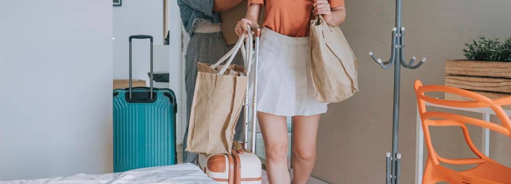 Woman moving home after treatment holding bag with suitcases behind her